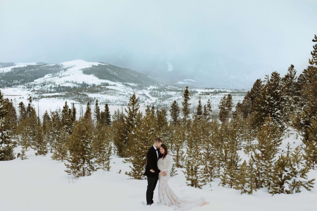 Bride and groom embracing surrounded by trees, mountains, and snow