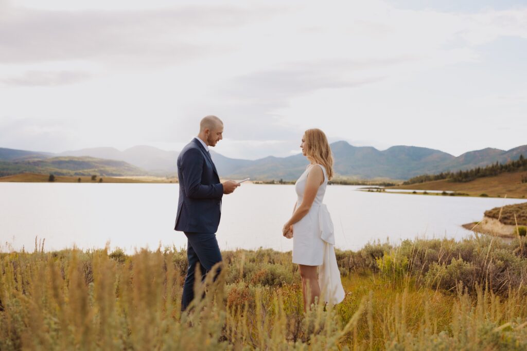 Groom reading vows to bride next to lake in Steamboat Springs