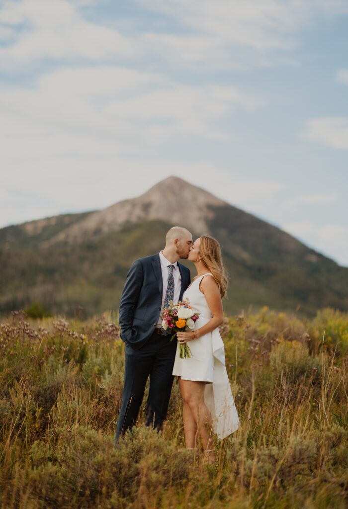 Bride holding flowers and kissing groom in front of mountain