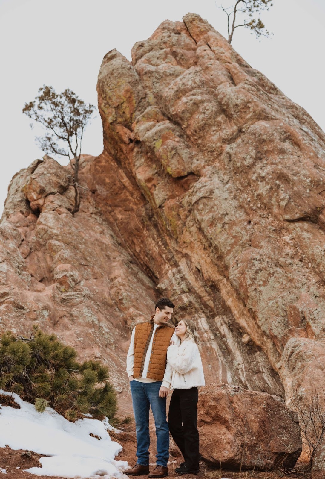 Couple looking at each other and standing in front of red rock for couples photography in Denver