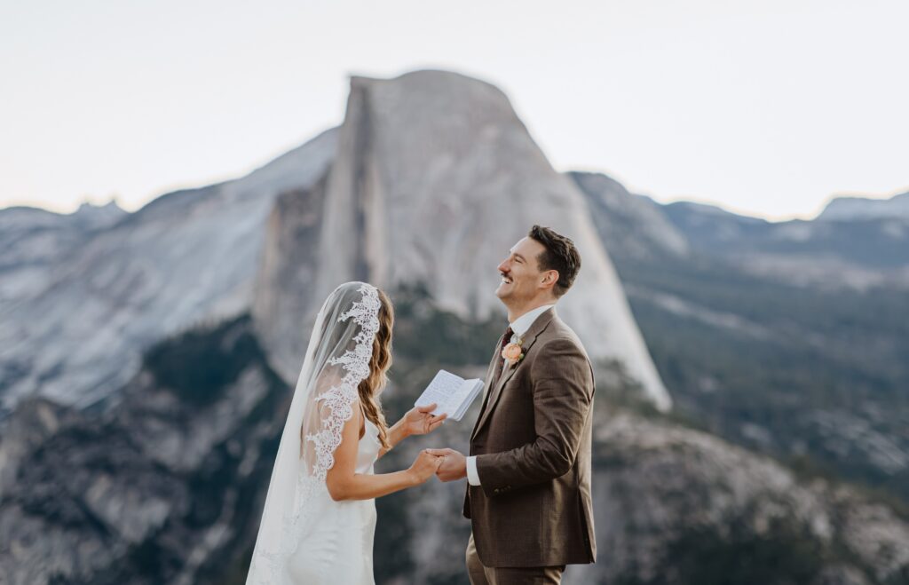 Groom laughing while bride reads vows at Yosemite National Park wedding next to mountain