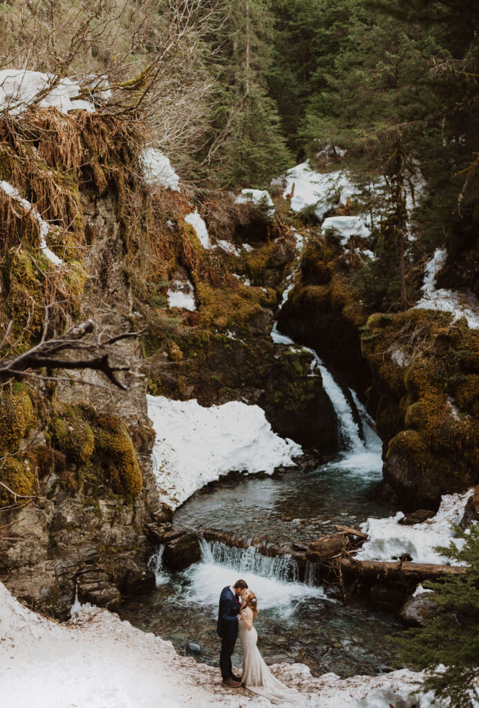 Bride and groom kissing at the base of a snowy waterfall in Alaska