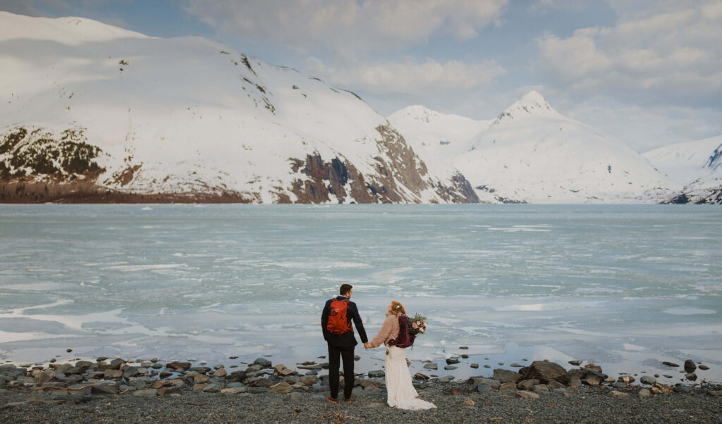 Bride and groom looking at snowy mountains and water for Alaska elopement