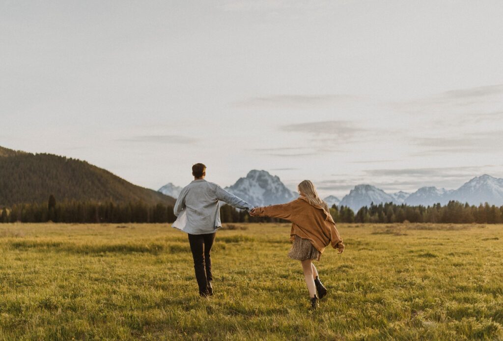 Couple holding hands and walking towards mountains at Grand Teton National Park