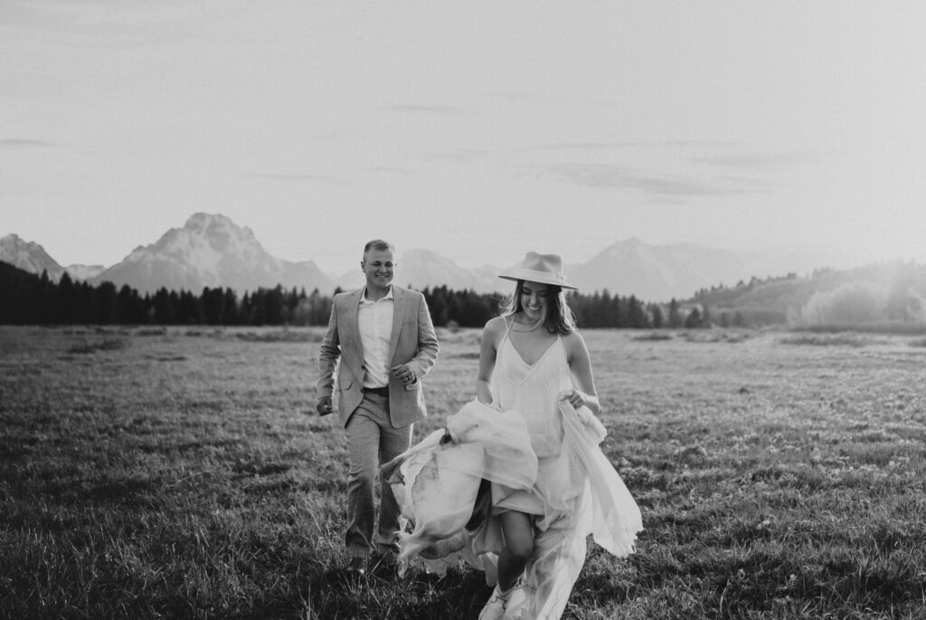 Couple smiling and running in field at Grand Teton National Park