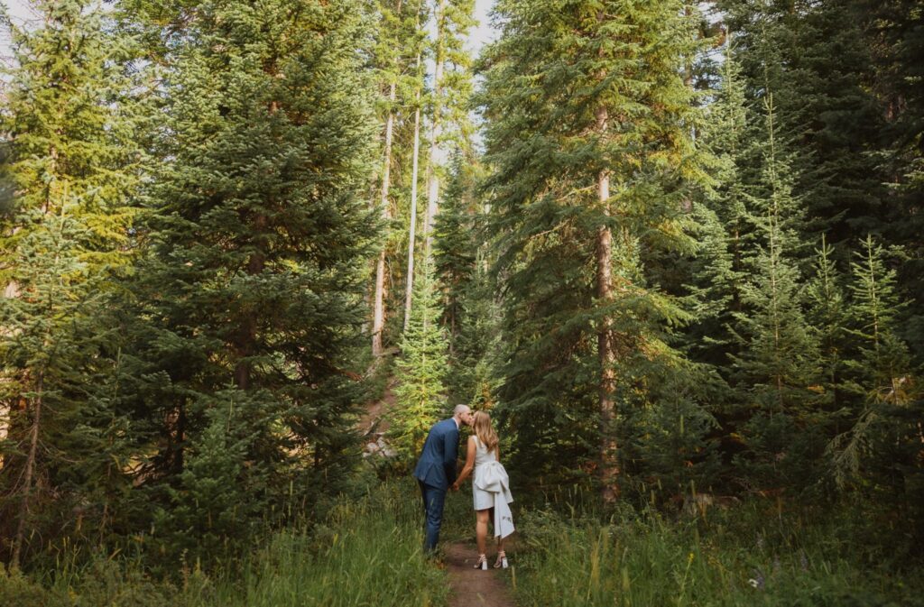 Bride and groom share a kiss while surrounded by pine trees