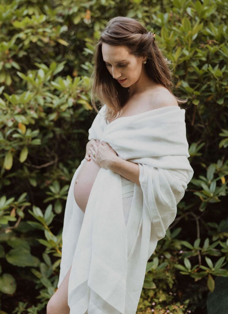 Pregnant woman holding belly standing in front of greenery
