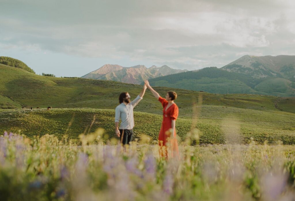 A couple dances among wildflowers with mountains in background during a Crested Butte proposal.