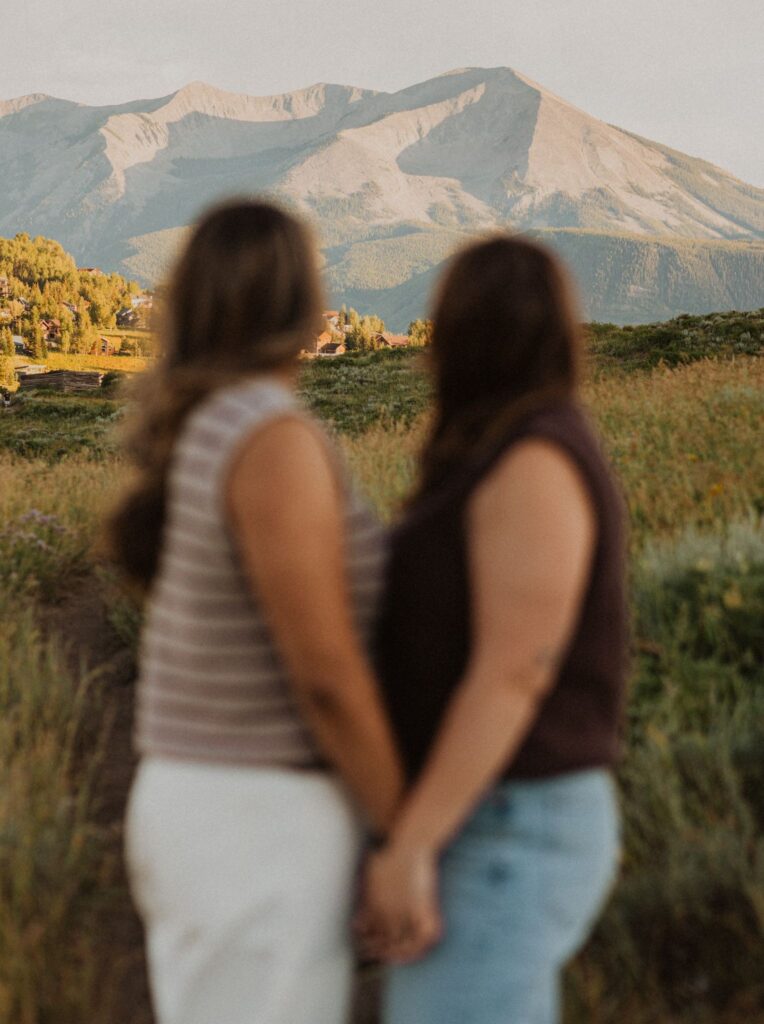 Couple holding hands and looking off to mountains in the distance during a Crested Butte proposal.
