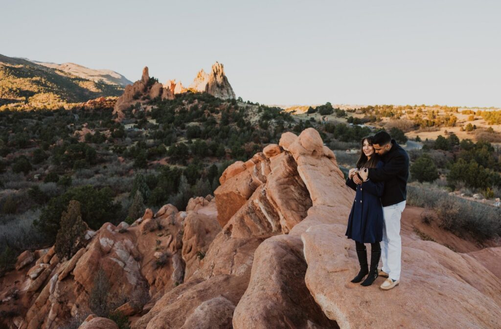 Man embraces woman from behind during Colorado proposal on red rock formations.