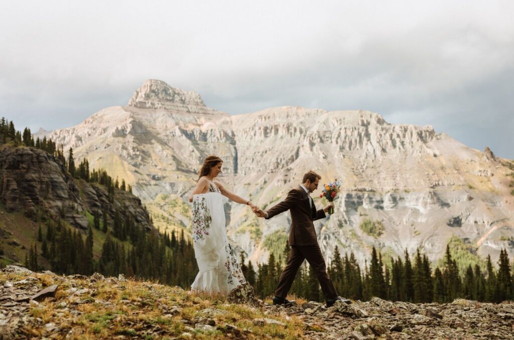 Groom leads bride by the hand with mountains in the background during a Gold Mountain Ranch wedding.