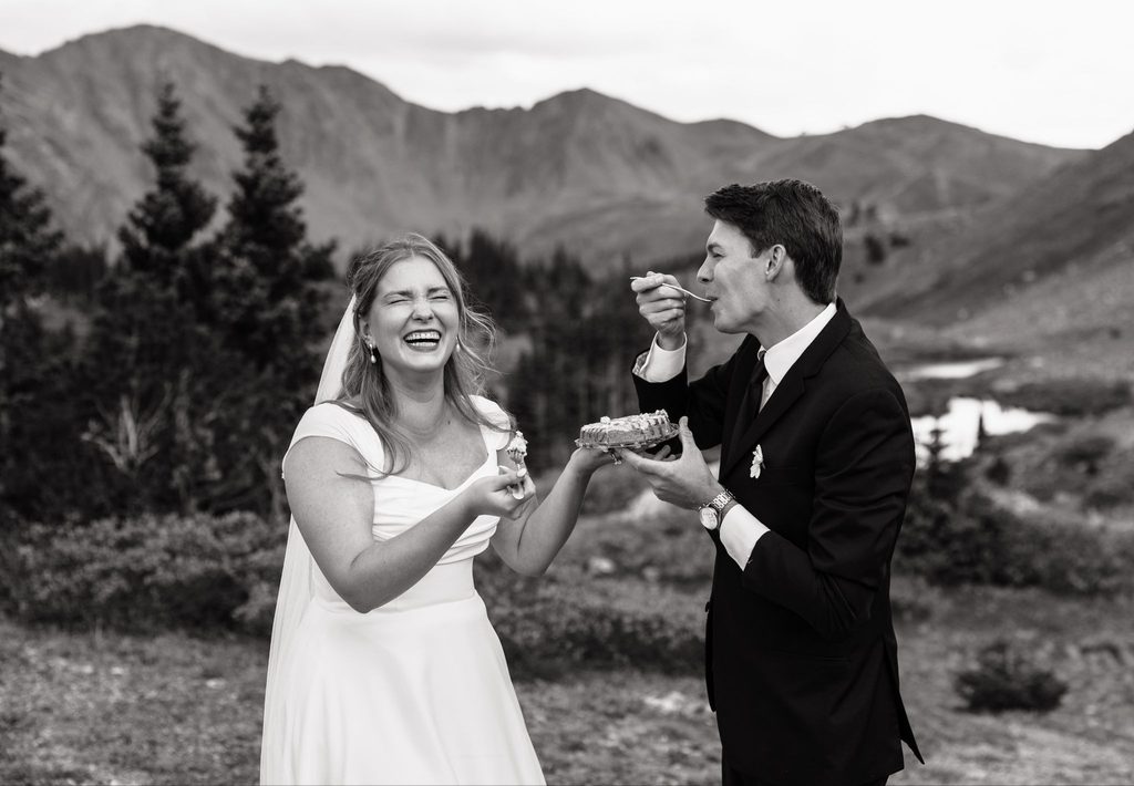 Black and white image of bride and groom eating cake and laughing.